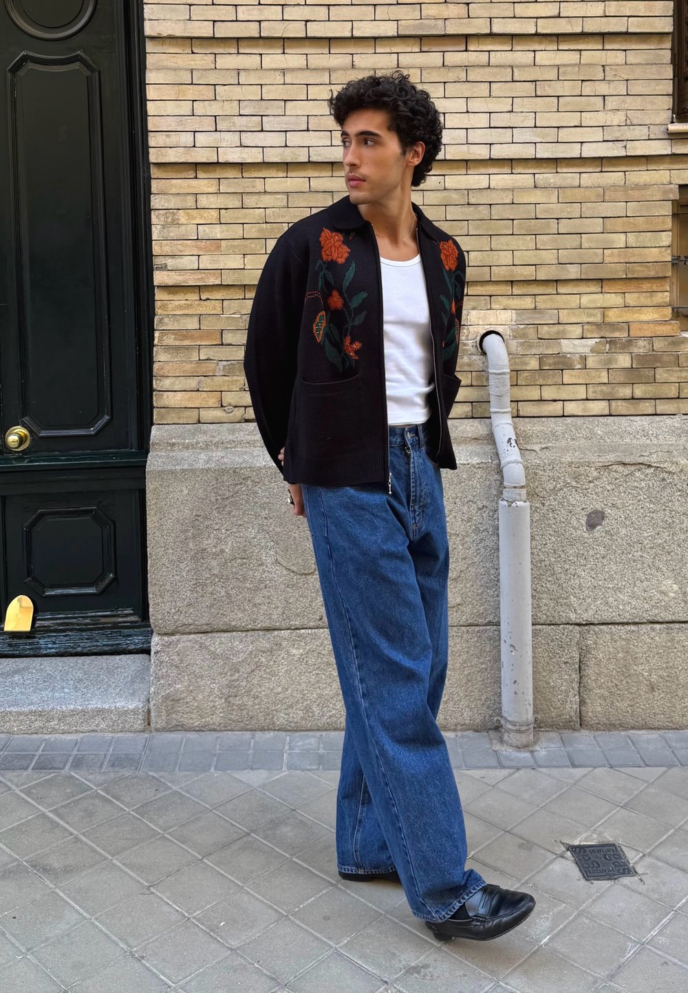 Čierny pletený cardigan s kvetinovou výšivkou, biele tričko a modré široké džínsy. Outfit dopĺňajú čierne topánky. Mesto, mestské prostredie.