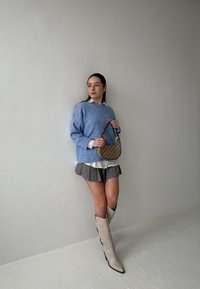 Světle modrý pletený svetr přes bílou košili s límečkem, šedá plisovaná sukně a béžové vysoké boty po kolena. Doplňky: malá hnědá kabelka.