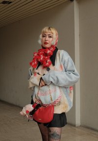 Maglione grigio oversize con trame colorate e morbide e design grafico. Gonna nera, sciarpa a quadri rossa e borsa rossa con catena dorata.