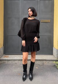 Μαύρο φόρεμα με μακριά, πρησμένα μανίκια, σμιλευμένη μέση και ρυτιδωτό στρίφωμα. Συνδυασμένο με μαύρες μπότες μέχρι το γόνατο και ατσάλινο χοντρό κολιέ.