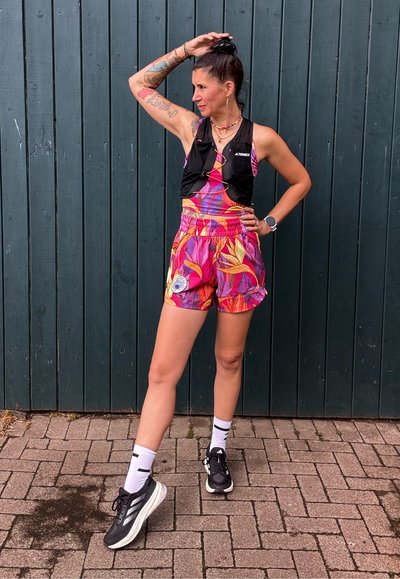 Conjunto deportivo colorido que incluye un top corto floral y pantalones cortos a juego. Un chaleco negro, zapatillas negras y calcetines blancos con rayas negras.