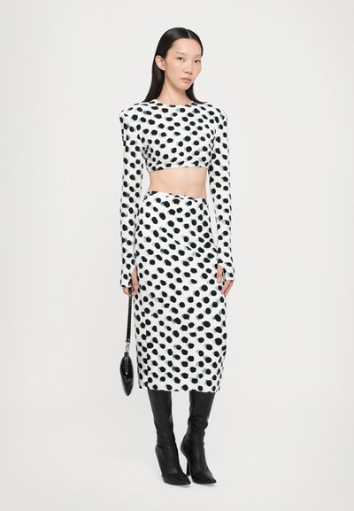 Conjunto de top corto y falda en un patrón de lunares en blanco y negro. Manga larga y diseño ajustado. La modelo sostiene un pequeño bolso negro.