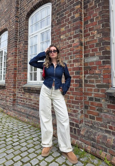 Chaqueta de mezclilla con un diseño ajustado y mangas acampanadas, combinada con pantalones anchos blancos y calzado de plataforma marrón. Acento de bolso rojo.