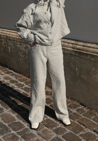 Completo a due pezzi grigio chiaro e strutturato, composto da un giubbotto corto con bottoni automatici e pantaloni a gamba larga. Indossato con scarpe bianche a punta quadrata.