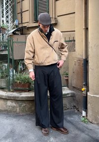 Bež kord jakna s črnim ovratnikom, žepi z zadrgo. Črne široke hlače. Rjavi čevlji s debelimi podplati. Siva kapa z ravnim vrhom. Mesto okolje.