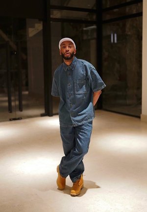 Conjunto de denim que incluye una camisa de botones de manga corta y un pantalón a juego, combinado con botas amarillas hasta el tobillo. Ambientado en un espacio interior.