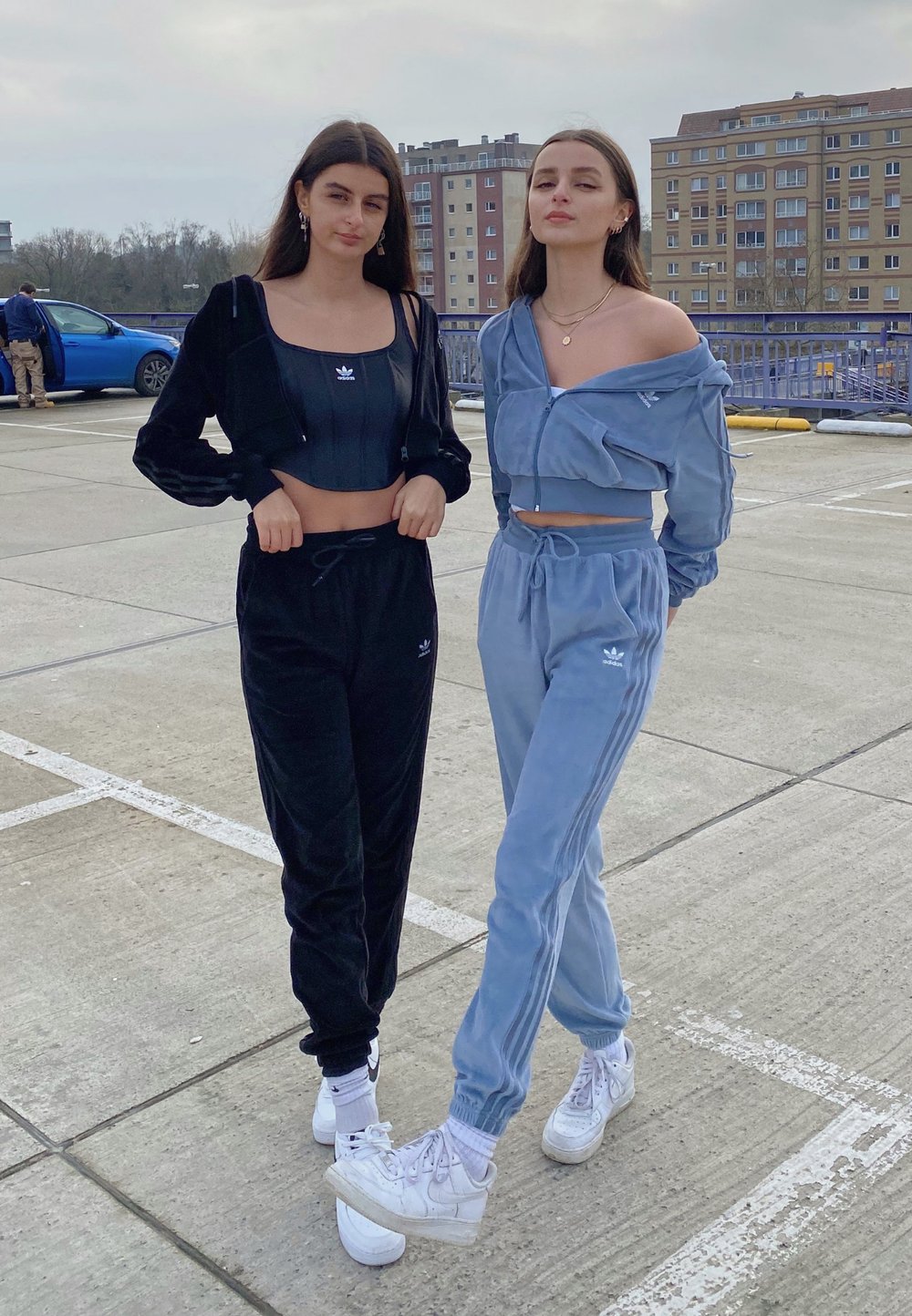 Két modell egyező laza tréningruhát visel; az egyik fekete bársonyból, a másik világoskékből készült, mindkettő crop toppal és fehér sportcipővel.