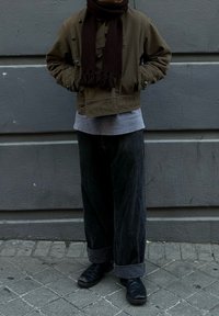 Odava roheline lühike jakk, hall pusa, laiad mustad püksid ja mustad kingad. Tumedat värvi sall narmastega lisab detaile. Kantud tekstuurse pinna peal.