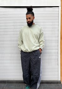 Sweatshirt verde claro oversize e calças pretas com estampa de leopardo e riscas brancas, com detalhe de logótipo. A pessoa está em pé contra um fundo de persianas.