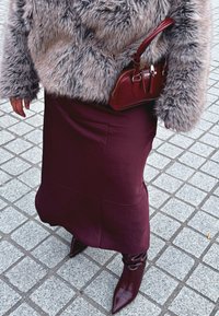 Casaco de pelúcia cinza, saia de cetim bordô e botas de bico fino a condizer. Pequena bolsa burgundy com fechos e detalhes.