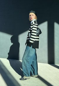 Μπλούζα με μαύρες και λευκές ρίγες, χαλαρούς μπλε τζιν, μαύρο μπερέ, μικρή μαύρη τσάντα και μαύρα παπούτσια. Ισχυρές σκιές σε γκρι φόντο.