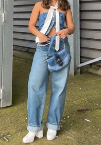 Džínový crop top s bielymi stužkami, svetlomodré široké nohavice a lesklé biele šľapky na blokovom podpätku. Malá modrá kabelka so zlatými akcentmi.