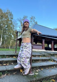 Kamuflažne cargo hlače svijetlosive boje s ljubičastim detaljima, uparene s krojenim maslinasto-zelenim crop topom i lavandom beanie; trendi tenisice upotpunjuju izgled.