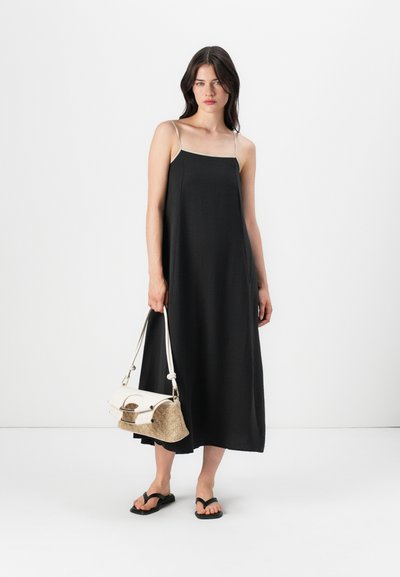 Vestido largo negro con tirantes finos, escote recto y ajuste holgado. Combinado con chanclas negras y un bolso blanco de dos texturas y paja.
