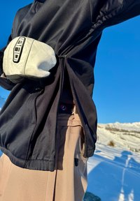 Top attivo nero con aperture laterali regolabili, abbinato a pantaloni color tan chiaro con una toppa con logo e tasca laterale.