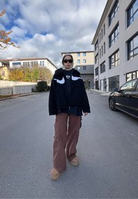 Μαύρο φλις μπουφάν με λευκές λεπτομέρειες, γκρίζα κουκούλα, μαύρο μπλουζάκι, καφέ cargo παντελόνι και μπεζ παπούτσια με πλατφόρμα σε έναν δρόμο.