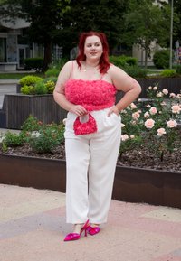 Rózsaszín rózsás textúrájú crop top fehér széles szárú nadrággal párosítva, rózsaszín flitteres táskával a kezében, amelyet fukszia színű magassarkú cipőkkel egészít ki.