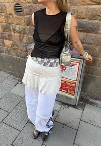Fekete átlátszó felső, fehér, csipkés szegélyű szoknya fölé rétegezve, fehér nadrággal, fekete csíkokkal és barna cipőkkel kombinálva. Ezüst kézitáska is tartozik hozzá.