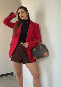 Rød blazer over en sort turtleneck, parret med brune shorts med pailletter. Grå håndtaske med brune accenter, guldhardware og en struktureret form.