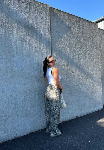 Pantalones de pierna ancha con estampado de leopardo y una textura suave, combinados con una camiseta sin mangas blanca ajustada. Los accesorios incluyen un pequeño bolso transparente.