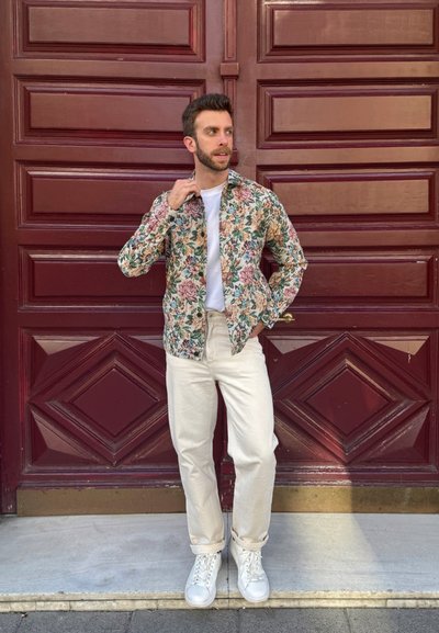 Chaqueta de patrón floral en color crema, con flores verdes, rosas y amarillas. Combinada con una camiseta blanca, pantalones beige y zapatillas blancas.