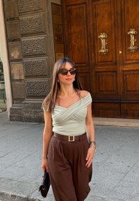 Svetlozelena bluzo brez naramnic z teksturirano tkanino, v kombinaciji z visokim pasom rjavih hlačami z zlatim zaponko. Rjava torba in sončna očala.