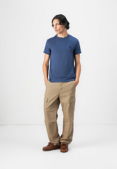 Camiseta de algodón azul marino con cuello redondo y pequeño logo, combinada con pantalones cargo color beige que cuentan con bolsillos laterales y corte recto.