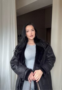 Palton negru cu guler de blană, combinat cu un top gri mulat. Textură netedă a țesăturii, nasturi mari și design simplu.