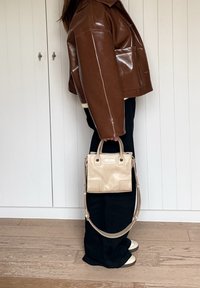Brown leather cropped jacket, black trousers, and beige handbag with top handles and shoulder strap, featuring a smooth texture and structured shape.