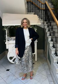 Jupe à sequins argentée, associée à un top blanc texturé et un blazer noir ajusté. Comporte des talons métalliques et un petit sac à main scintillant.