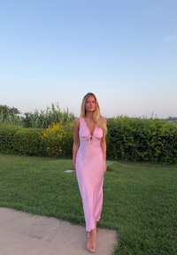 Světle růžové bezramínkové šaty s hlubokým výstřihem a detailem uvázání na prsou. Měkká látka s hladkým povrchem. Jsou nošeny naboso na trávě.