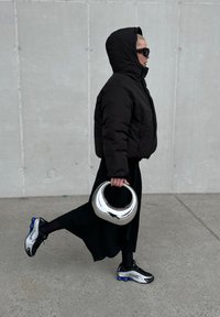 Casaco de puffer preto, saia longa preta, bolsa metálica prateada, óculos de sol e ténis estampados com detalhes em preto e azul.