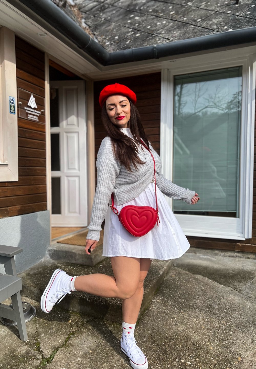 Vitt klänning med utsvängd nederdel, grå ribbad tröja, röd hjärtformad handväska, röd basker och vita sneakers med mönstrade strumpor.