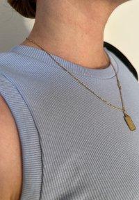 Top senza maniche a coste di colore azzurro chiaro con scollatura rotonda, abbinato a una collana in oro con un pendente rettangolare.