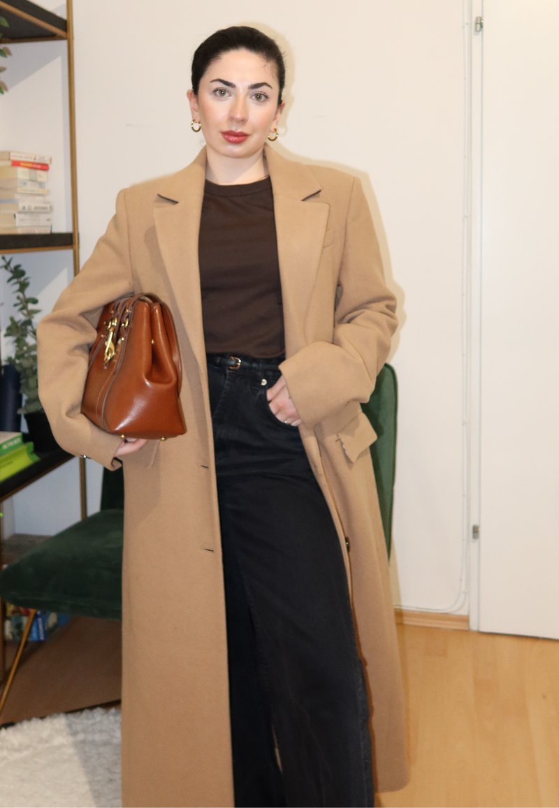 Beežist villast mantel kohandatud lõikega, kombineeritud pruuni topi ja kõrge vöökohaga mustade teksadega. Käes pruuni nahast käekott.