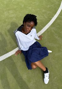 Camisa de manga larga de Adidas con rayas verticales y cuello negro, combinada con una falda azul marino y zapatillas deportivas blancas con detalles en negro.