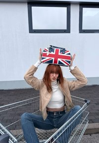 Round handbag featuring a Union Jack design in red, white, and blue, with black accents and a star charm, held above the model's head.