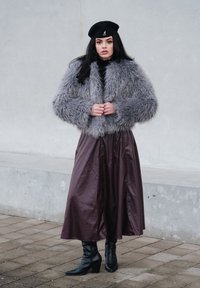 Veste en fausse fourrure grise, longue jupe sombre, béret noir et bottes noires à talons montant jusqu'aux genoux. Matériau texturé et design en couches.