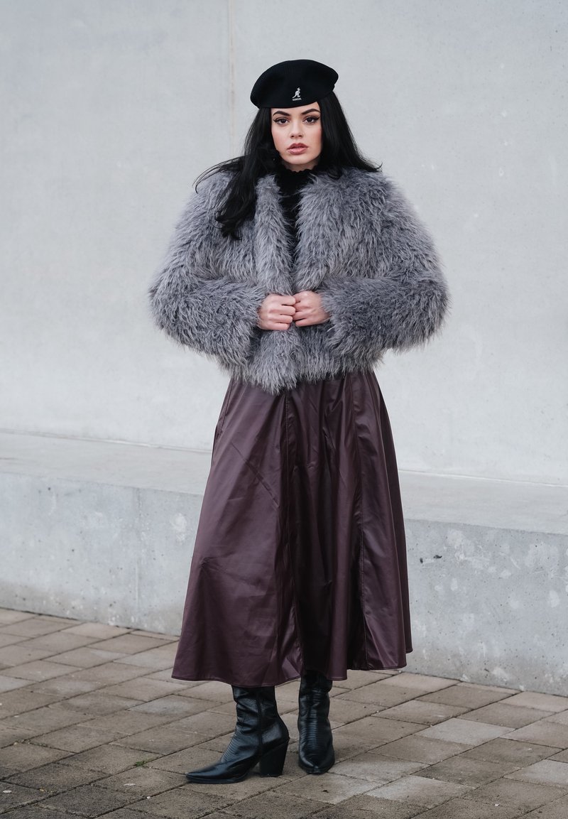 Veste en fausse fourrure grise, longue jupe sombre, béret noir et bottes noires à talons montant jusqu'aux genoux. Matière texturée et design en couches.