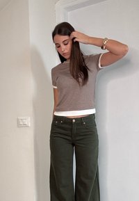 Bruine top met korte mouwen en witte rand, gecombineerd met hoge taille broek in donkergroen met wijde pijpen. Eenvoudig ontwerp; stof lijkt zacht en katoenachtig.