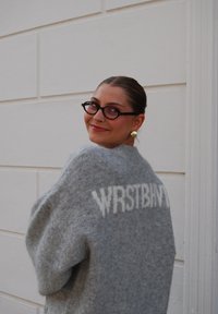 Grå strikkegenser med oversized passform, med teksten "WRSTBHVR" i hvitt på baksiden. Myk tekstur og design med senket skulder.