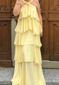 Gelbes Chiffonkleid mit geschichteten Rüschen, Halterneck-Design, Chiffonrose-Akzent, fließende Silhouette und glatte Textur.
