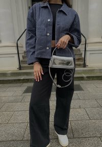 Námornícky pruhovaná skrátená bunda so striebornými gombíkmi, kombinovaná s čiernymi širokými nohavicami a metalickou kabelkou s reťazovým popruhom. Biele tenisky.