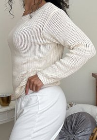 Suéter leve em malha, com mangas longas, trama texturizada e um corte descontraído, combinado com calças brancas.