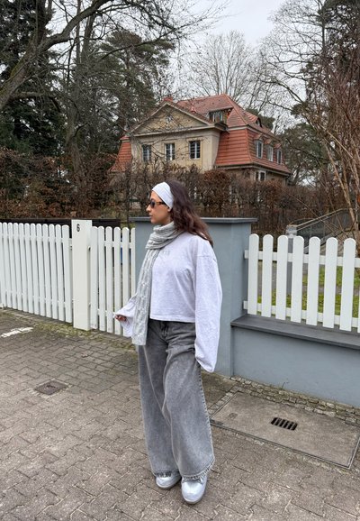 Sudadera corta de color gris claro y vaqueros anchos grises con una textura sobredimensionada. Zapatillas plateadas y una bufanda gris con estampado completan el conjunto.