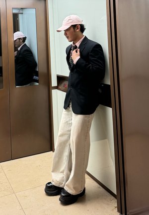 Persona que lleva puesta una blazer negra sobre una camisa rosa clara y una corbata estampada, combinada con pantalones crema de gran tamaño y zapatos de plataforma negros y brillantes.