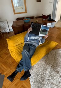 Fauteuil lounge jaune rembourré avec tissu textur é ; personne lisant un magazine. Mobilier en bois environnant et un bol d'oranges visibles.