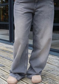 Sive denim široke hlače s izblijedjelom teksturom, s slobodnim krojem i vidljivim šavovima, u kombinaciji sa bež obućom.