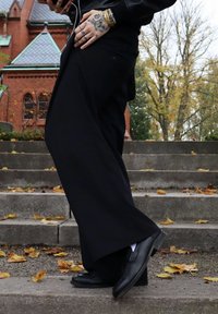 Sorte bukser med vide ben kombineret med sorte sko. Stoffet virker glat, og outfittet har lagdelte detaljer samt en afslappet pasform.