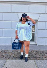 Άσπρο φόρεμα με στενή μέση, μπλε και άσπρο ριγωτό oversized πουκάμισο, μαύρο καπέλο, ναυτικό tote bag με λογότυπα και μαύρες loafers.